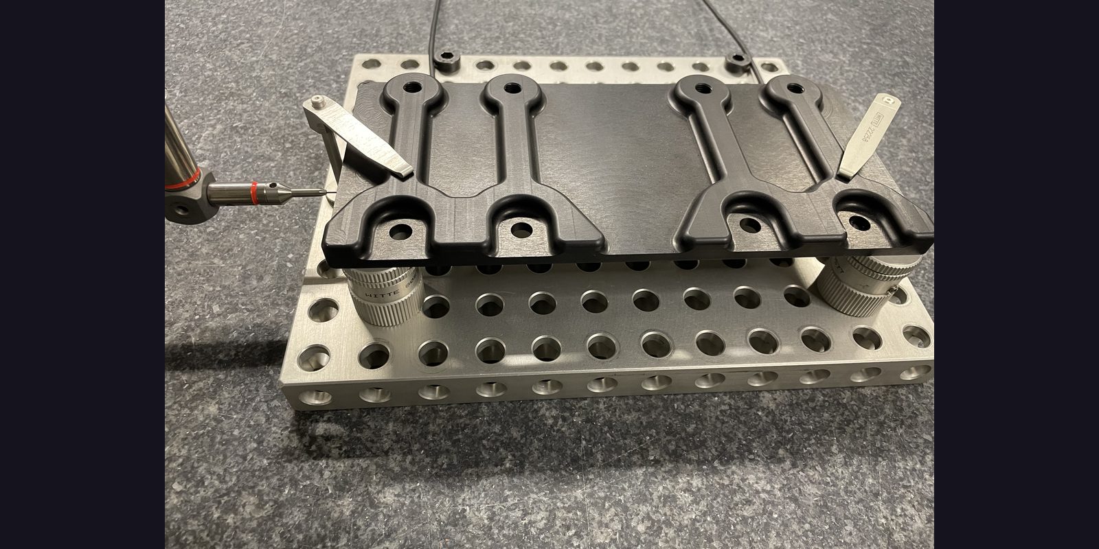 Stichprobenprüfung im Wareneingang — Serie schwarzer Hebel-Bauteile auf Aufspannraster mit taktilem Tastkopf, Lieferantenkontrolle nach AQL und Charge-Freigabe
